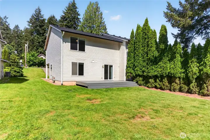 Rear exterior showcases the duplex’s spacious yard, deck, and private setting bordered by mature evergreens. Plenty of room to spread out outdoors while enjoying the peaceful cul-de-sac location close to Lake Tapps amenities and Church Lake Park access.