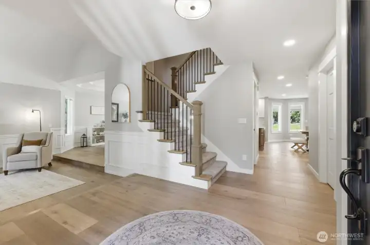 Bright foyer sets the tone with wide-plank hardwood floors, elegant wainscoting, soaring ceilings, and a beautifully crafted staircase with iron balusters. Abundant natural light enhances the open-concept design, creating a seamless flow to the home's living spaces. Thoughtful architectural details and quality finishes offer a sophisticated first impression and an inviting sense of home from the moment you step inside. Bright foyer sets the tone with wide-plank hardwood floors, elegant wainscoting, soaring ceilings, and a beautifully crafted staircase with iron balusters. Abundant natural light enhances the open-concept design, creating a seamless flow to the home's living spaces. Thoughtful architectural details and quality finishes offer a sophisticated first impression and an inviting sense of home from the moment you step inside.