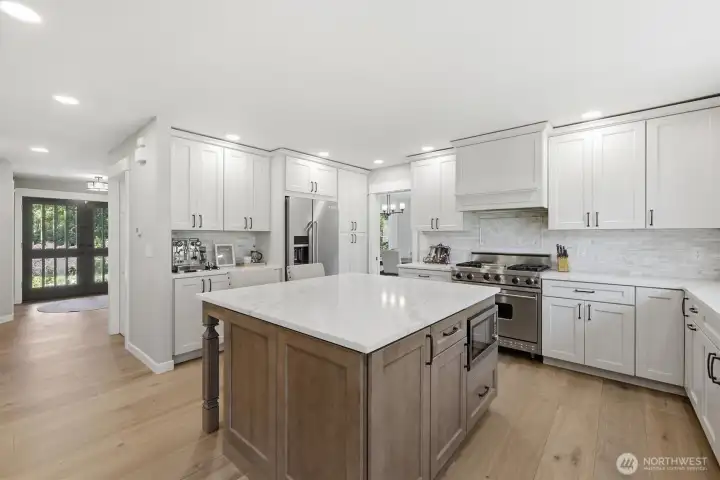 The designer kitchen showcases crisp white cabinetry, slab stone countertops, stainless steel appliances, a large center island with seating, and stylish tile backsplash. The designer kitchen showcases crisp white cabinetry, slab stone countertops, stainless steel appliances, a large center island with seating, and stylish tile backsplash.