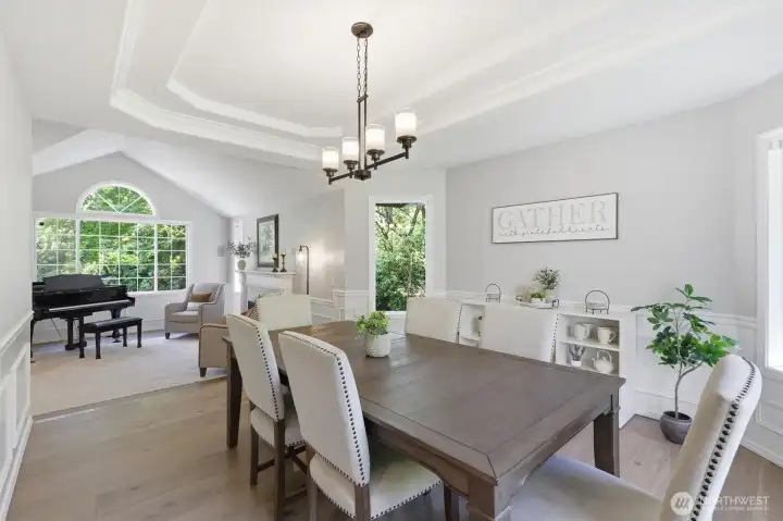Gather and entertain in style in this elegant formal dining room featuring detailed wainscoting, crown molding, tray ceiling, and rich hardwood floors. Large windows frame serene greenery views and fill the space with natural light, while the open sightlines create a seamless flow for hosting. A warm, inviting setting that blends timeless craftsmanship with modern comfort. Gather and entertain in style in this elegant formal dining room featuring detailed wainscoting, crown molding, tray ceiling, and rich hardwood floors. Large windows frame serene greenery views and fill the space with natural light, while the open sightlines create a seamless flow for hosting. A warm, inviting setting that blends timeless craftsmanship with modern comfort.