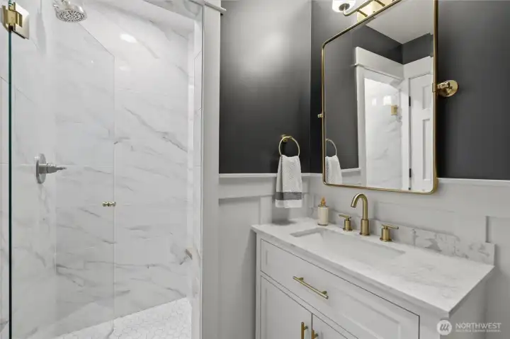 Main floor ¾ bath featuring a walk-in shower. Custom vanity is topped with quartz countertops and complemented by designer lighting, gold fixtures and rich accent walls, and timeless millwork details. A sophisticated blend of style and function, thoughtfully updated for guests and everyday convenience. Main floor ¾ bath featuring a walk-in shower. Custom vanity is topped with quartz countertops and complemented by designer lighting, gold fixtures and rich accent walls, and timeless millwork details. A sophisticated blend of style and function, thoughtfully updated for guests and everyday convenience.