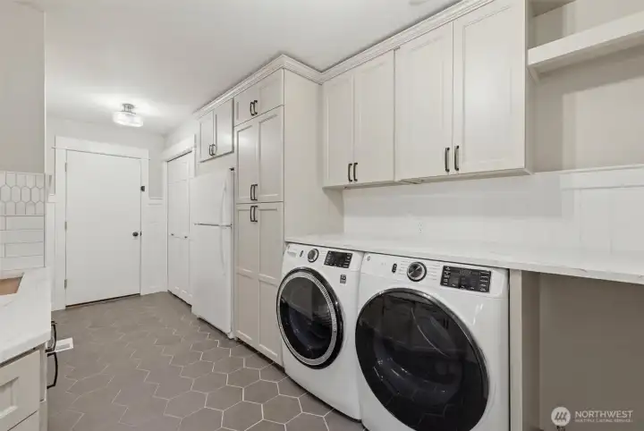 Laundry and mud room offers abundant storage, extensive countertop workspace, and a convenient utility sink. Extra refrigerator and custom cabinetry stretches to the ceiling, providing exceptional organization, while durable designer tile flooring stands up to busy household traffic. A perfect drop zone for coats, shoes, backpacks, and pets, this hardworking space blends practicality with the same high-end finishes found throughout the home. Laundry and mud room offers abundant storage, extensive countertop workspace, and a convenient utility sink. Extra refrigerator and custom cabinetry stretches to the ceiling, providing exceptional organization, while durable designer tile flooring stands up to busy household traffic. A perfect drop zone for coats, shoes, backpacks, and pets, this hardworking space blends practicality with the same high-end finishes found throughout the home.