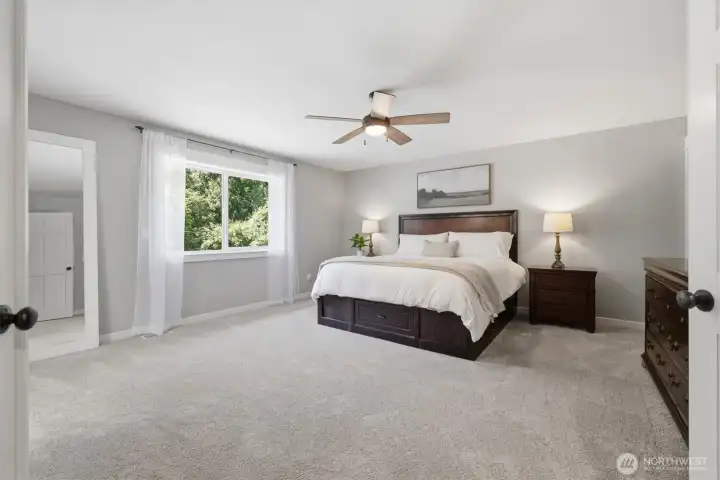 Unwind in the generous primary suite, a peaceful retreat featuring expansive proportions, plush newer carpeting, and large picture windows that frame serene views of the surrounding greenery. Adjacent walk-in closet and primary bath Unwind in the generous primary suite, a peaceful retreat featuring expansive proportions, plush newer carpeting, and large picture windows that frame serene views of the surrounding greenery. Adjacent walk-in closet and primary bath
