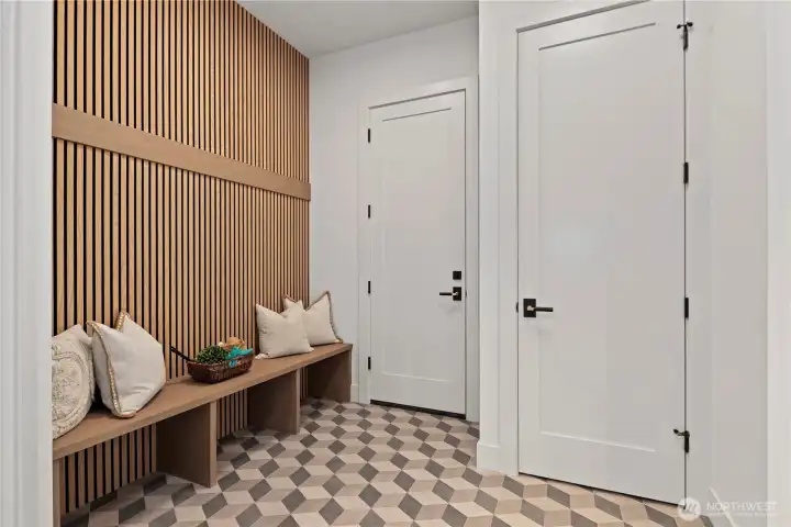 Thoughtfully designed mudroom with custom bench, 3D geo tile floor pattern, slat accent wall detail, coat hooks (will be installed, and coat closet. .