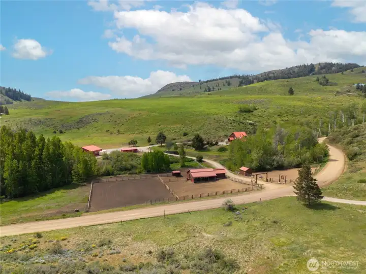 Lovely Upper Rendezvous setting showcasing the full layout, open arena, barns, paddocks, and the home privately set among aspens, surrounded by rolling hills, wild flowers and wide Methow Valley skies.