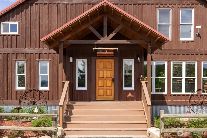 Welcoming front entry with classic western character—timber-framed covered porch, rich cedar siding, and a warm wood front door create an inviting first impression, complemented by thoughtful landscaping and rustic accents that reflect the property’s authentic country charm.