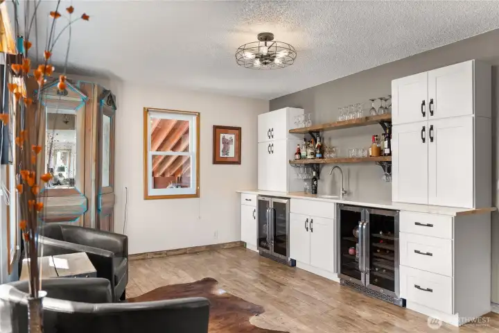 Welcome.... entry with bar to the left and great room to the right.  Enjoy this stylish and functional entertaining space with custom cabinetry, dual wine refrigerators, open shelving, and wet bar—perfect for hosting with a relaxed Western flair.