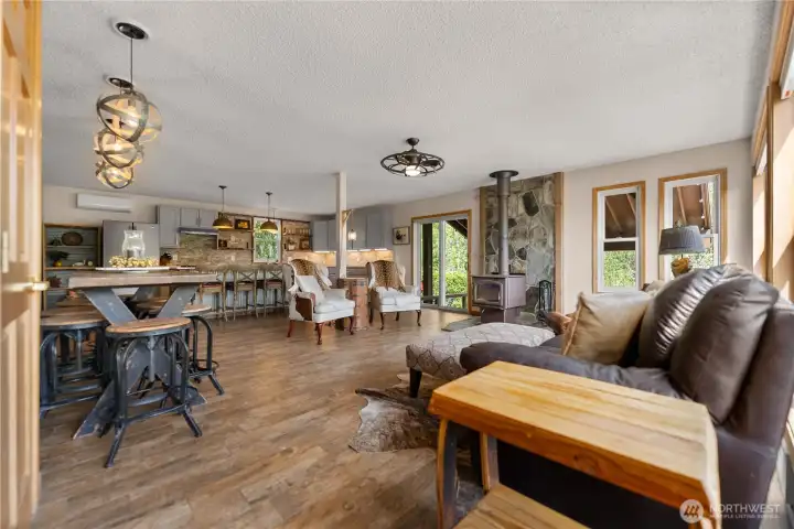 Open great room design seamlessly connects dining, living, and kitchen areas, anchored by a cozy wood stove and framed by sliding doors that extend the living space to the covered patio—ideal for relaxed everyday living and effortless entertaining.