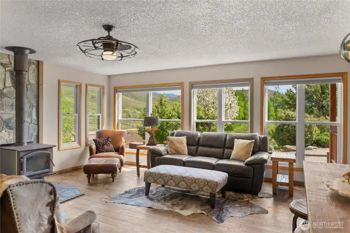 Warm and inviting living space centered around a wood stove with stone hearth,, where expansive windows frame the surrounding hillsides and bring the outdoors in.