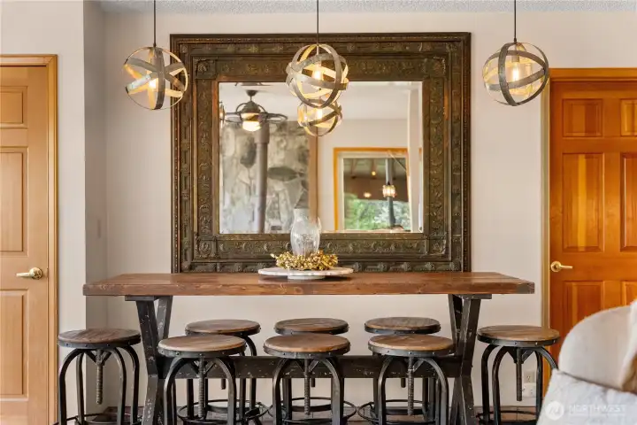 Artistic dining bar with rustic wood top and industrial-style seating, set beneath statement lighting and anchored by a large framed mirror that adds depth and character.  All furnishings negotiable.