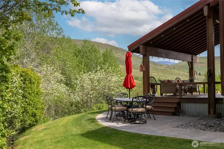 Covered outdoor living overlooking the property, with a spacious deck and paver patio set along the aspen grove—ideal for dining, relaxing