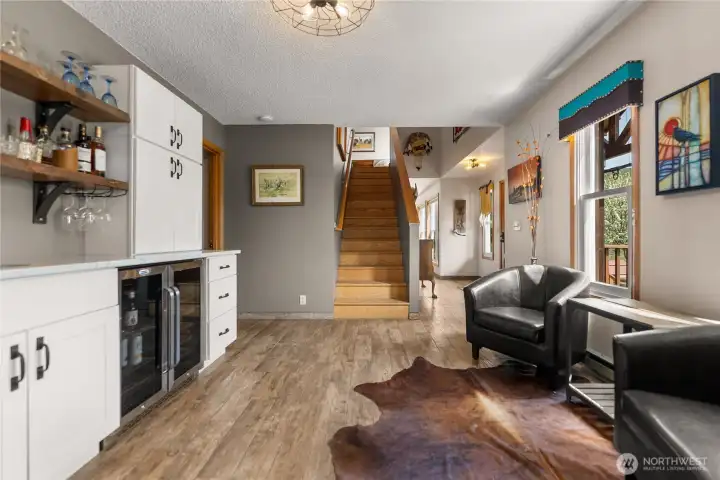 Welcoming main entry foyer featuring a stylish wet bar, warm wood staircase to the second level, and a relaxed sitting area that sets the tone for this inviting home.