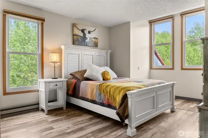 Large light-filled second bedroom with warm wood trim, clean finishes, and peaceful views, offering a comfortable and inviting space.