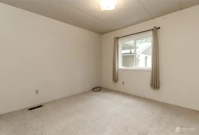 Extra bedroom with carpet and view of the back of the garage and side yard through this window.