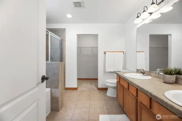 Primary bathroom with walk in shower, tub and 2 sinks. Looking into the walk in closet area.