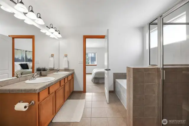 Primary bathroom with 2 sinks, tub and shower. Standing view from the primary closet.