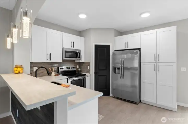 Modern open concept kitchen features white shaker cabinets, quartz countertops, stainless steel appliances, a pantry and plenty of storage.