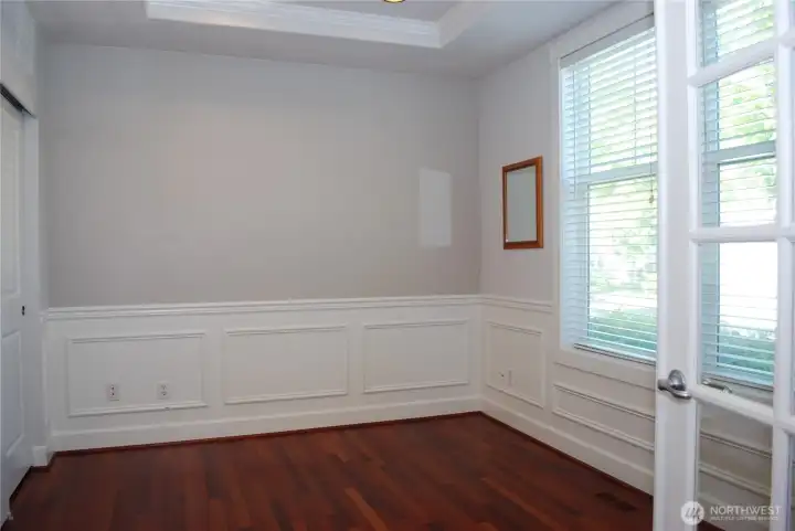 Brazilian cherry hardwood floors flow past the glass panel French doors in the 9 foot coffered ceiling, half wall panel style den.