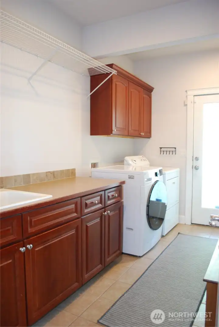 Large luxury utility room with natural light streaming through the glass door, 9 foot ceilings, sink, and plenty of storage and hanging space!