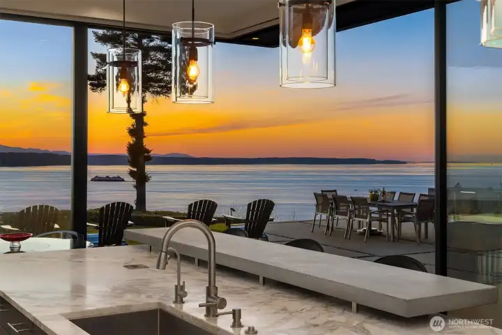 Designer chef’s kitchen opens directly to expansive waterfront terraces and sunset entertaining spaces through dramatic retractable glass walls.
