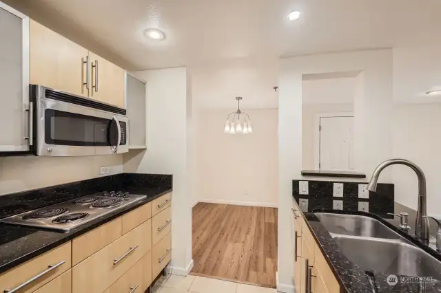 View of the kitchen facing the dining room, showcasing the electric cooktop, microwave, and several cabinets with translucent glass doors.