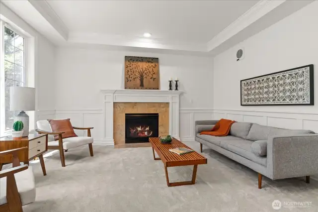 Intimate living room with cozy gas fireplace, coffered ceiling, and oversized window offering pleasant front yard views