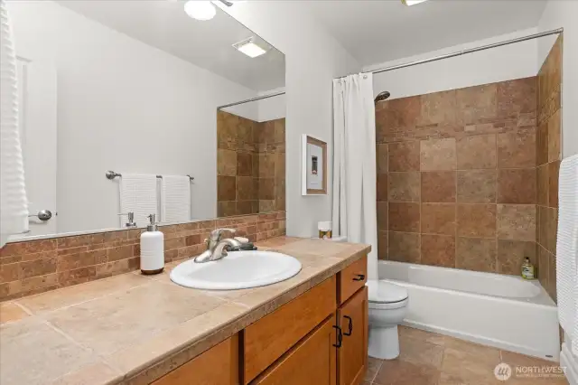 upstairs bathroom with elongated vanity with tub and tile surround