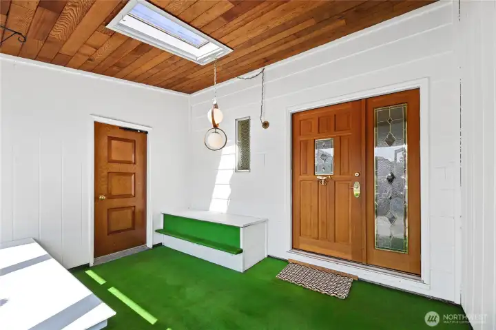 Front door to home with lead glass design window, opening sidelight with matching lead glass   Storm door entry  2 sitting benches  Wall to wall windows with blinds  Tongue & Groove ceiling with skylight  Entrance door to attached 2 car garage  Cat door