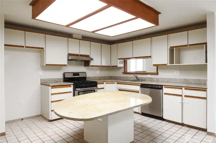 SPACIOUS KITCHEN  Large table height island with storage and electrical  Granite surfaces  Cream flat face cabinets with wood trim  Microwave cubby