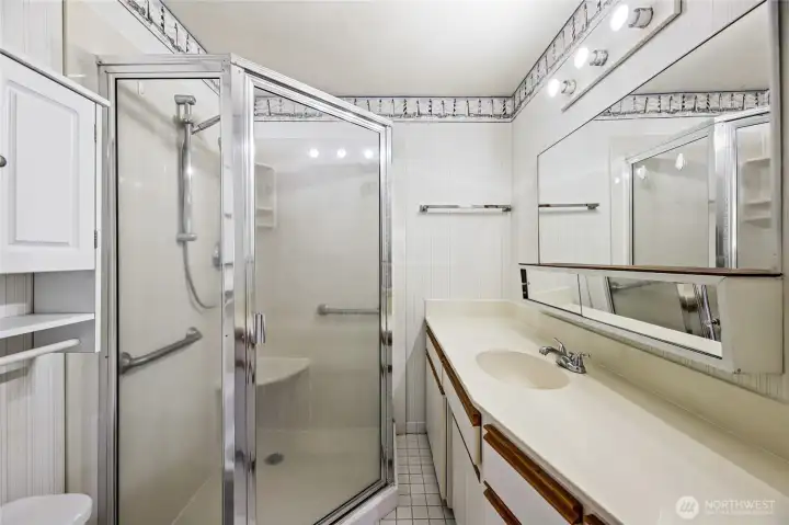 ¾ BATHROOM  Single sink vanity with cream flat face cabinets with wood trim  Large corner shower with shower wand and built-in seat  Tile floor / Pocket door entry