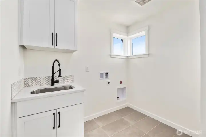 Laundry Room: Spacious laundry with upper cabinetry, utility sink, and tile flooring offers convenience and functionality. Washer and dryer are not included, allowing you to customize appliances to your preference.  These photos are of the actual, staged home being sold at Foxmoore. However, all photos, renderings, site maps, and floorplans are for visualization purposes only. Plans, colors, building orientation, finishes, home outlook, and other details can and WILL vary.
