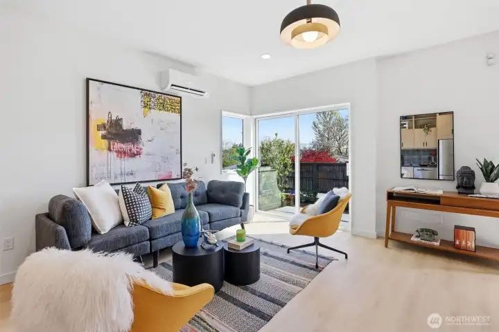 Bright open-concept living room with oversized windows, mini-split heating and cooling, natural light, and seamless access to private outdoor space.