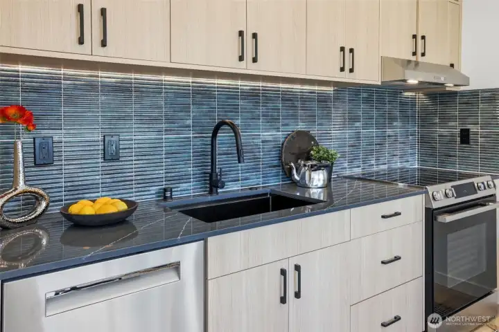 Designer kitchen with quartz countertops, custom cabinetry, stainless steel appliances, tile backsplash, and abundant storage.