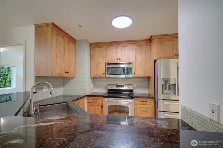 Well-appointed kitchen with slab granite surfaces & stainless-steel appliances.