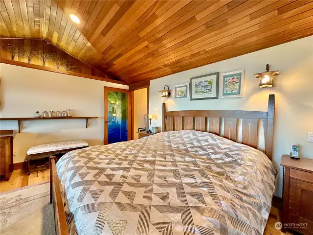 Spacious primary bedroom with vaulted ceilings and and artist’s glass primary bathroom door.