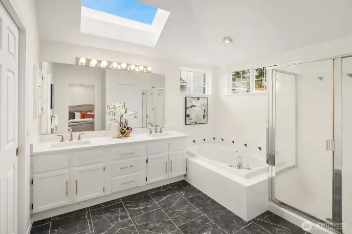 Large primary bathroom with walk in shower, tub, and double vanities. Skylights above keep the space light and bright. Walk in closet is just off the bedroom
