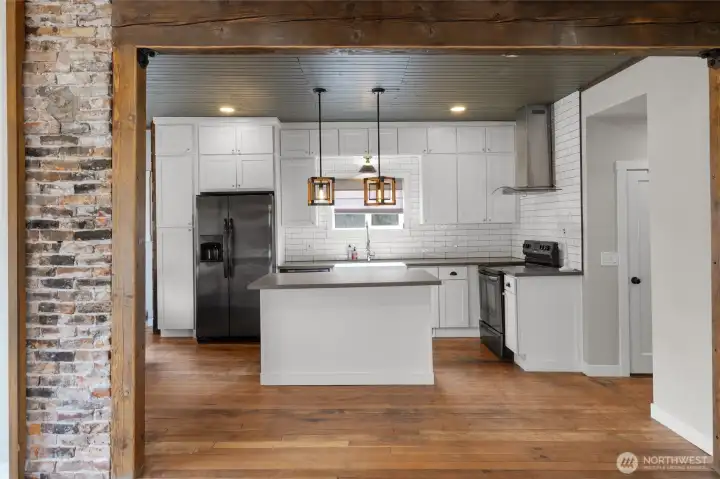 View from the living room into the kitchen, with front entry on the left and hall way to the right to main floor bedroom, bathroom, rear mud room and stairs to the lower level. The original floors, brick and beams in this home give it so much enchanting.