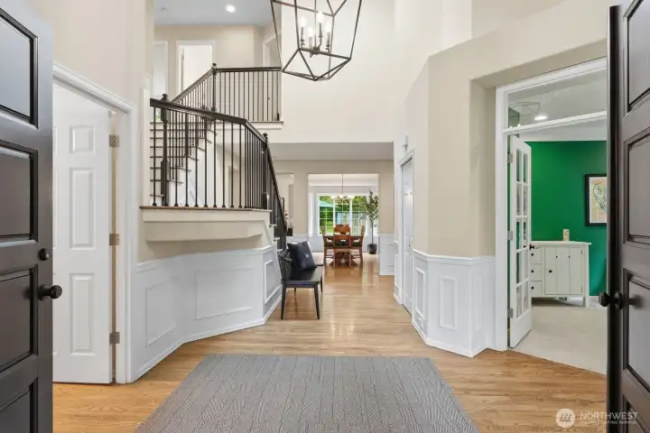 A dramatic foyer adorned with classic wainscoting, soaring ceilings, a statement chandelier, and a gracefully turned staircase with newly updated iron railings and hardwood treads.