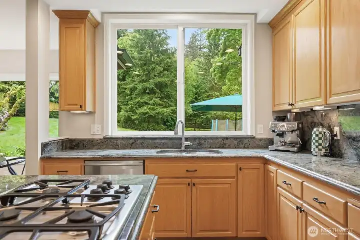 The chef’s kitchen is both stylish and functional, showcasing honey-toned maple cabinetry, slab granite countertops, stainless steel appliances, a generous center island with bar seating, and a walk-in pantry.