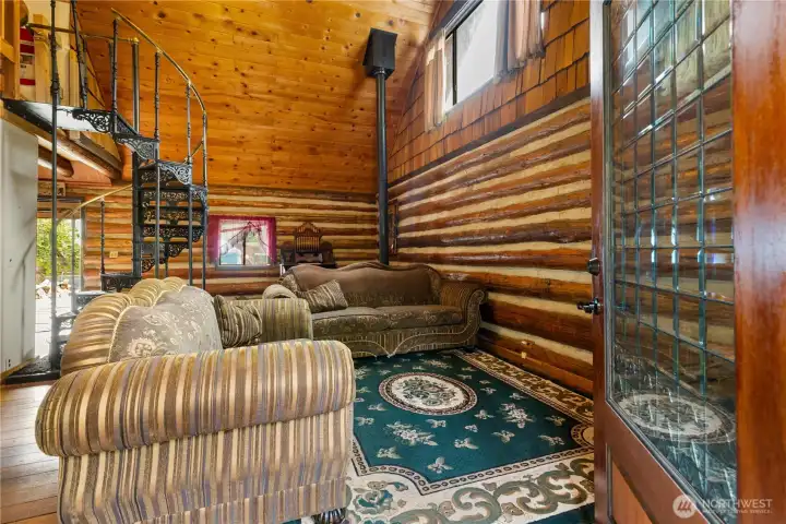 Detailed view of the intricate wrought-iron spiral staircase, a striking centerpiece connecting the main floor to the loft above, surrounded by log walls and vintage décor.