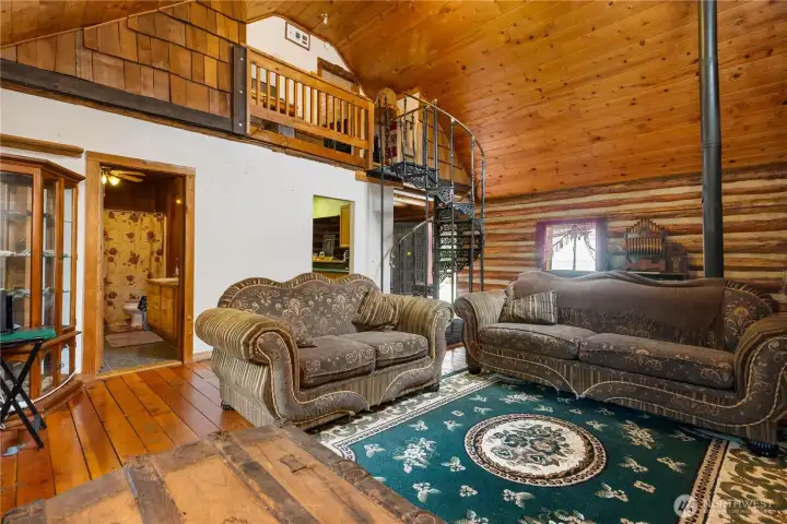Living room view highlighting the spiral staircase, loft railing, and direct access to the main floor bathroom. Exposed beams, natural wood finishes, and rustic details give this space authentic cabin charm.