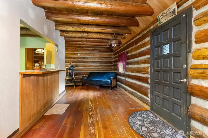 The wide-plank floors and hand-hewn log walls make the entry feel like stepping into a storybook lodge. A “Sasquatch Crossing” sign and cozy wood stove hint at the personality and history tied to this one-of-a-kind property.