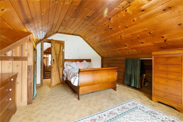 Alternate loft angle showing the warm wood finishes, built-in storage, and barn-style door. A comfortable and inviting space with room for a full bedroom setup.