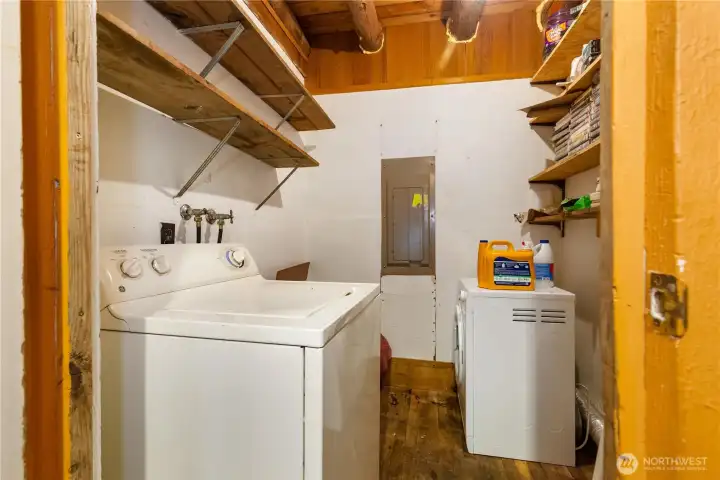 Compact laundry room with washer and dryer hookups, open shelving for storage, and exposed wood beams that tie into the rustic character of the cabin.