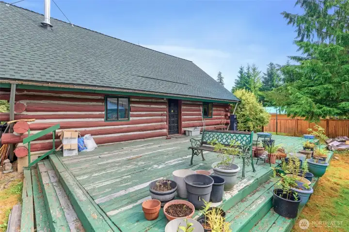 Spacious back deck offering plenty of room for outdoor living, container gardening, and entertaining. Surrounded by evergreens, this private outdoor space extends the rustic lifestyle of the log cabin.