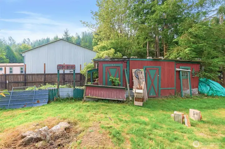 Cluster of rustic red outbuildings with green trim, including storage sheds and a playful “Boot Hill” sign. These structures add character while offering versatile space for projects, storage, or creative use.