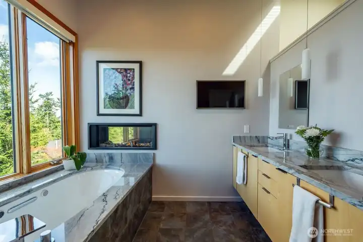 The primary suite bathroom, with heated tub, gas fireplace, quartzite counters, and frame tv.