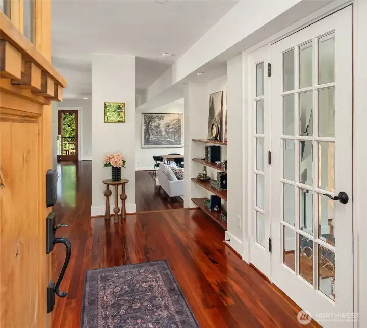 A grand hallway with tall ceilings and tigerwood floors. A flex room is to the right which could be a library, den, office, or TV room.
