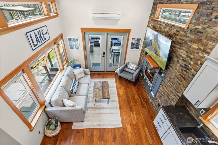 Open-concept living area with soaring ceilings, floor-to-ceiling stone fireplace, and large windows bringing in natural light. Open-concept living area with soaring ceilings, floor-to-ceiling stone fireplace, and large windows bringing in natural light.