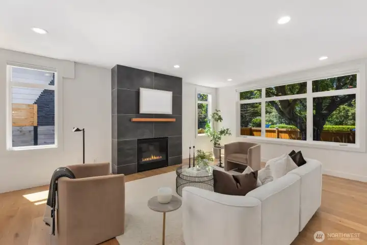 Sunlit living room with a gas fireplace and oversized windows overlooking the yard. Sunlit living room with a gas fireplace and oversized windows overlooking the yard.